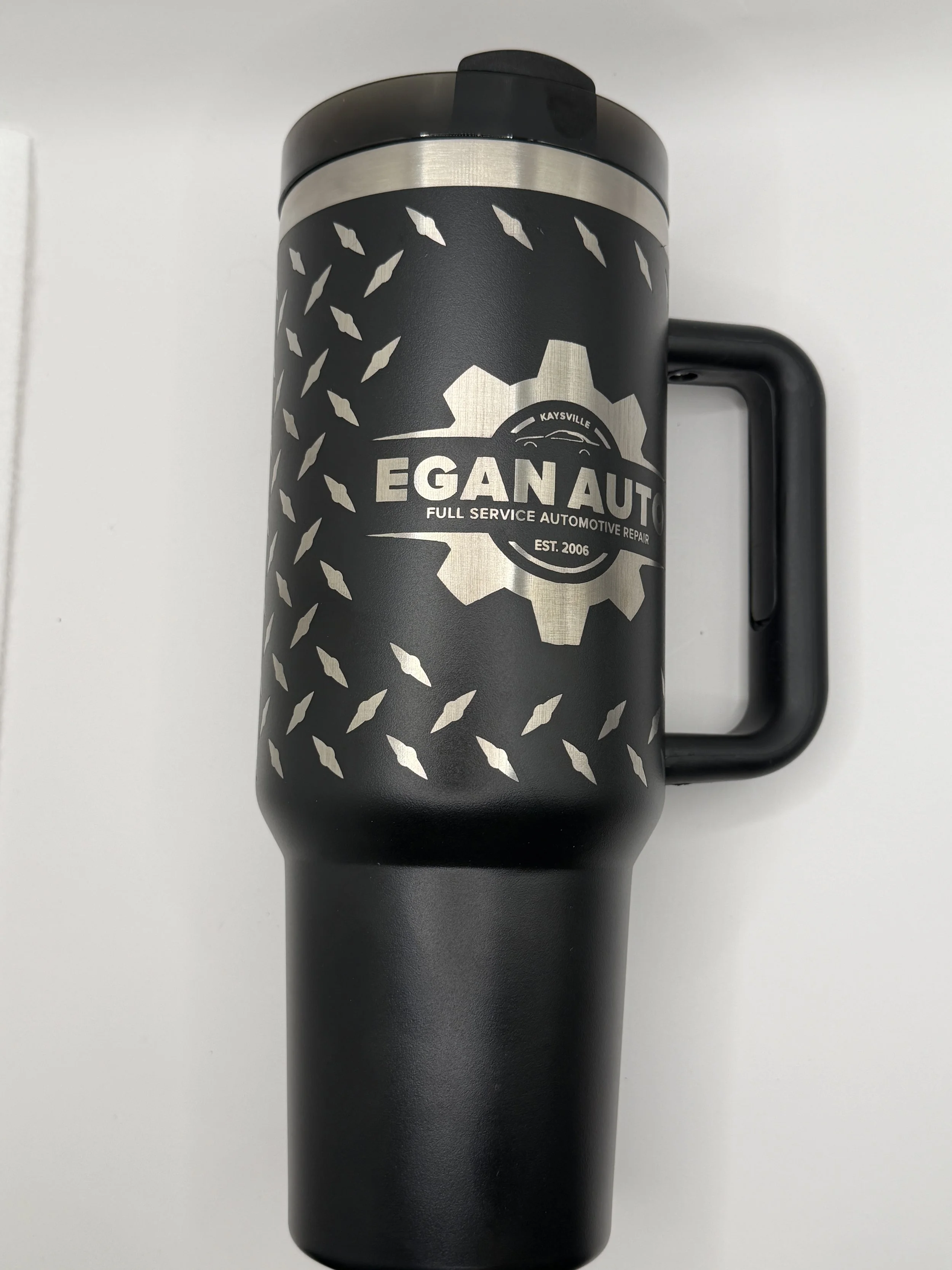 Black travel mug with a gear logo and the words 'Egan Auto Full Service Automotive Repair' printed on it, with a handle on the right side.