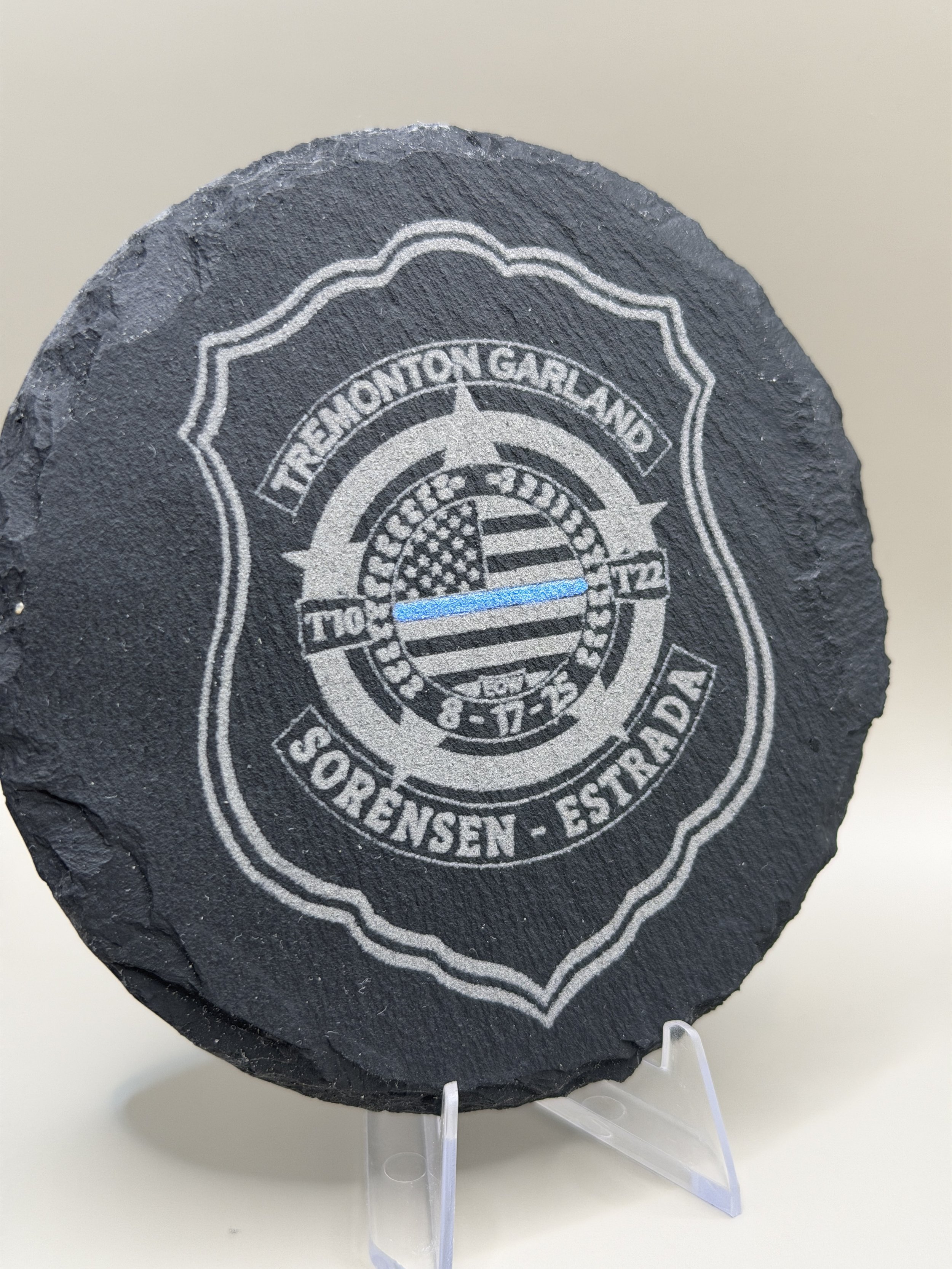 Black slate token with a white badge design, featuring the text "TREMONTVILLE TOWNSHIP POLICE" and "SOBREN - ESTRADE." The center has a circular emblem with an American flag and a star.