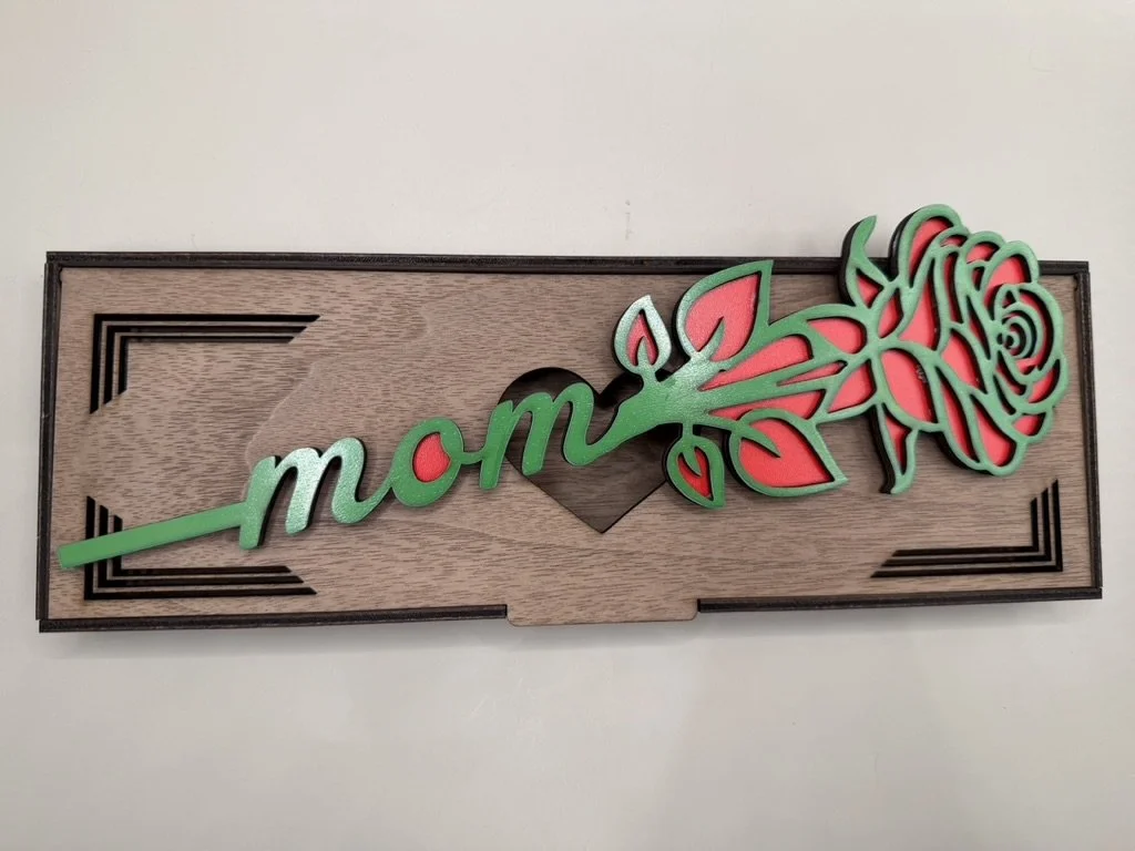 Wooden wall decor with the word "mom" and a pink rose design.