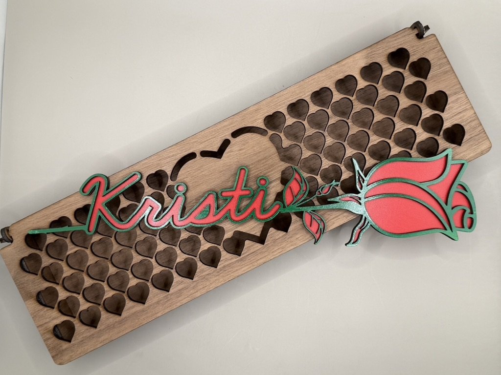 Decorative wooden board with heart-shaped cutouts, featuring a colorful neon sign that spells 'Kristi' and a stylized rose design.