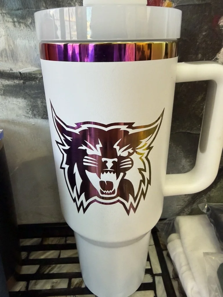 A white ceramic travel mug with a large handle featuring a fierce lion's head logo in dark purple and white.