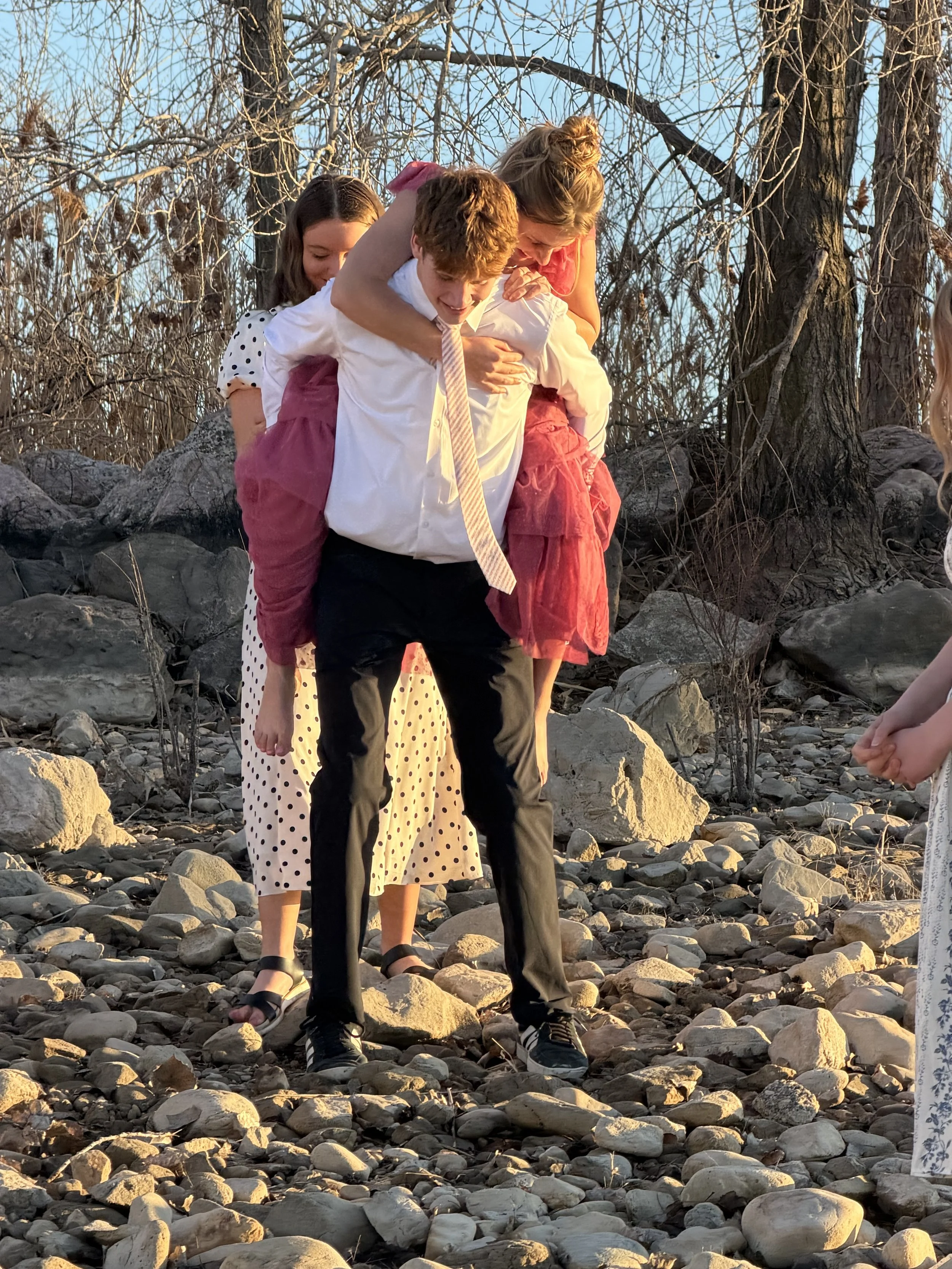 Friends playing on rocky terrain during sunset, with leafless trees in the background.