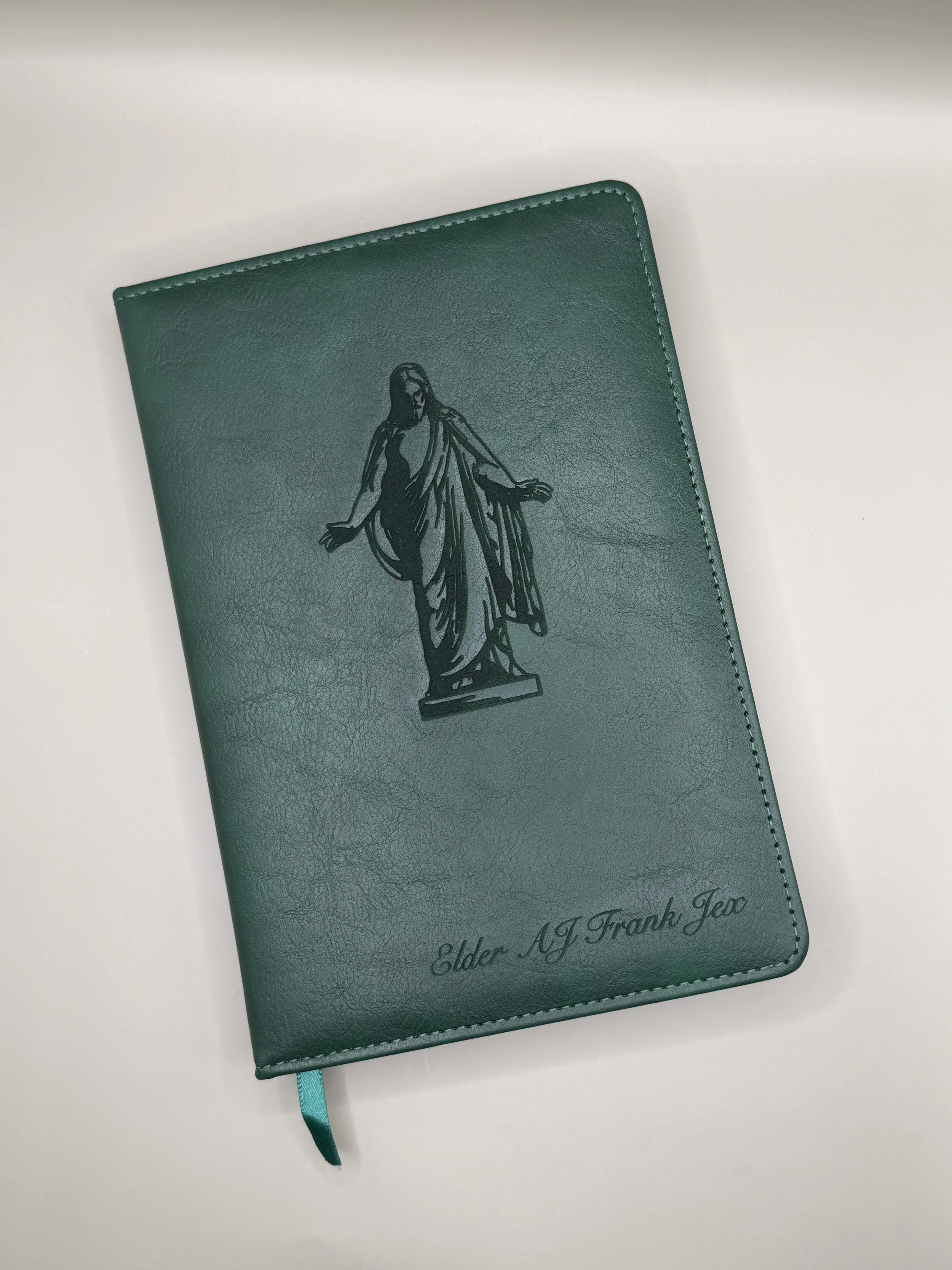 A green leather planner with a black illustration of Jesus Christ on the cover, and the words "Elder AJ Frank Jex" written at the bottom.