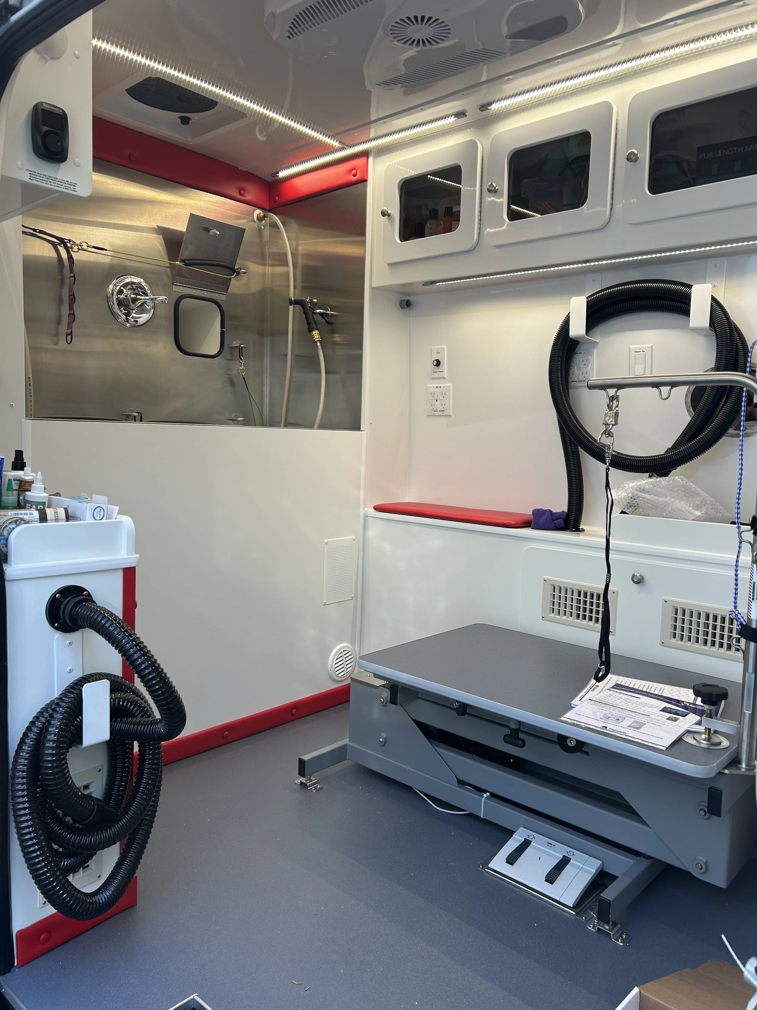 Inside of a mobile veterinary clinic with a grooming table, storage cabinets, and equipment for animal care.