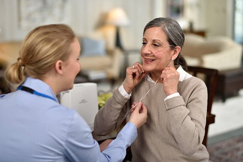A nurse helping an elderly woman put on a hearing aid in a cozy living room.