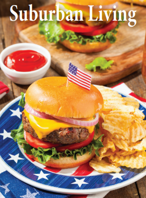 A plate with a cheeseburger topped with an American flag toothpick, surrounded by potato chips, with a burger and ketchup in the background.