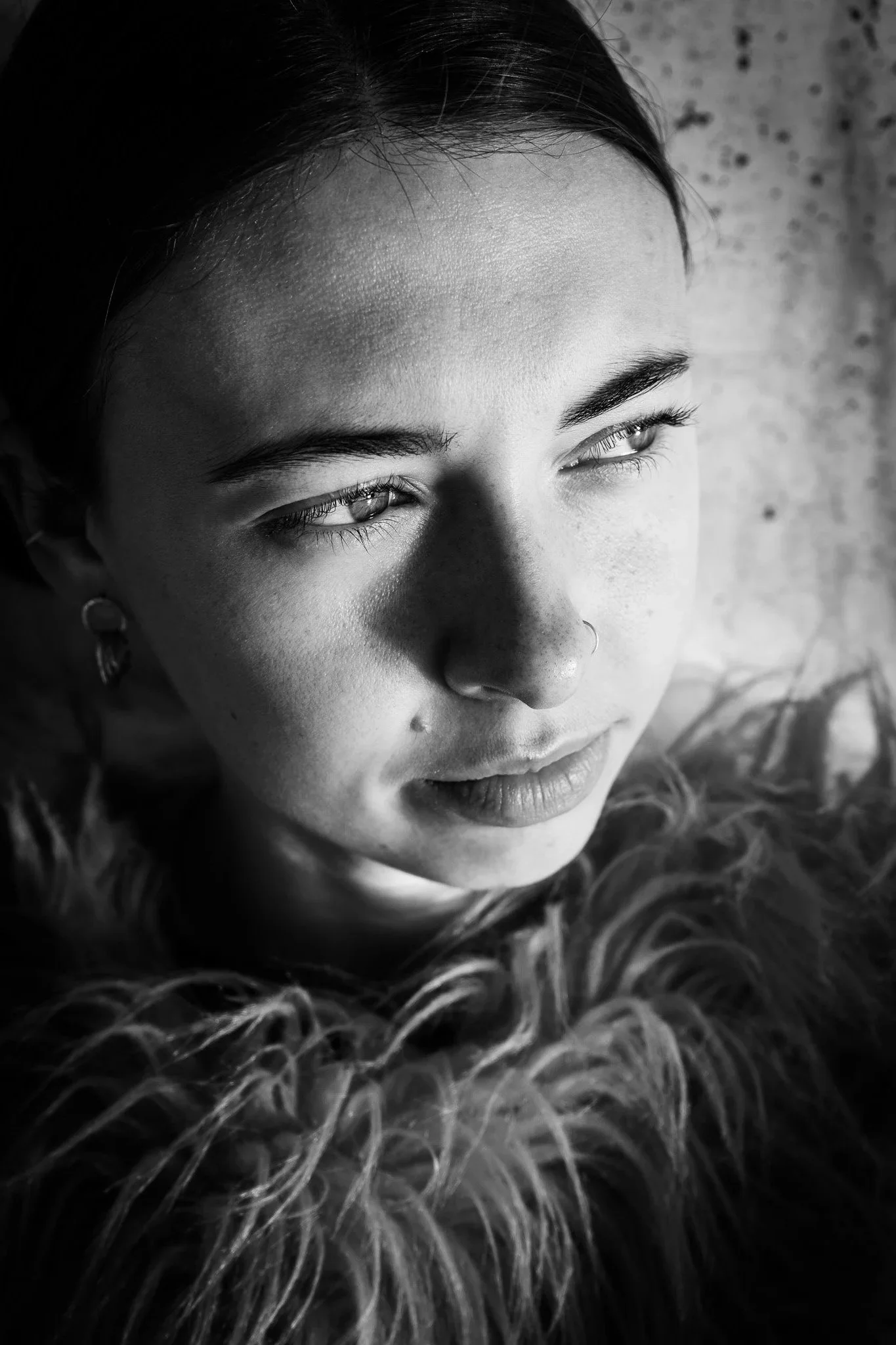 Close-up black-and-white portrait of a young woman with light eyes, dark hair, and piercings, looking slightly away from the camera.