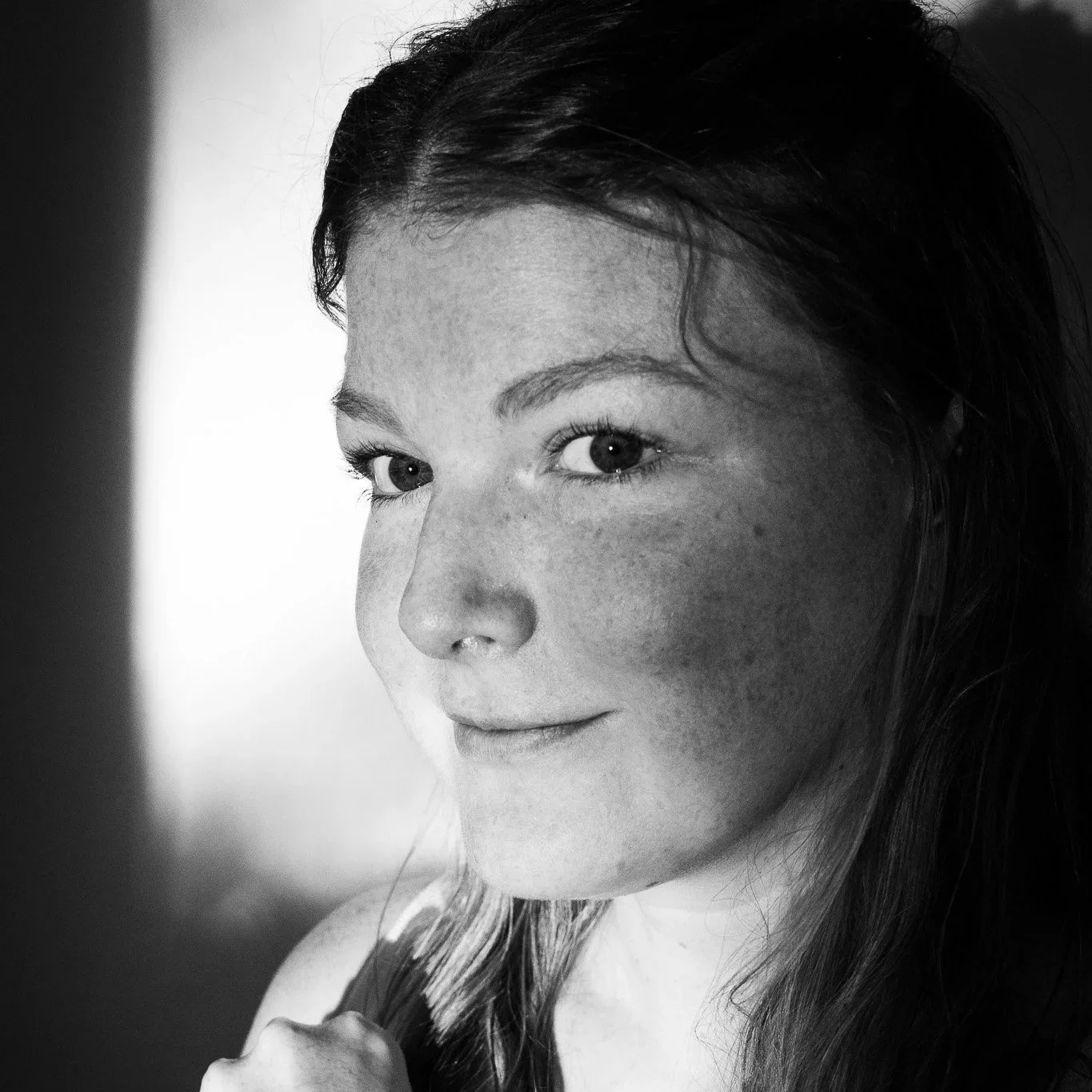 Close-up black-and-white portrait of a young woman with light eyes, dark hair, and piercings, looking slightly away from the camera.