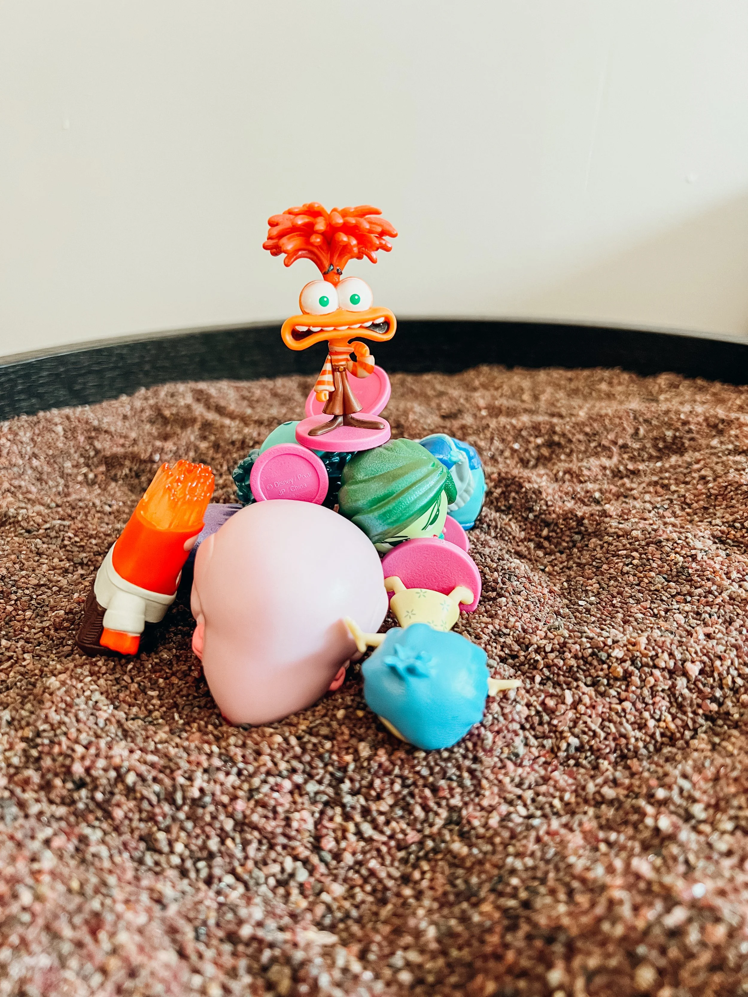 A pile of colorful toys on a textured surface with a cartoon character toy at the top.