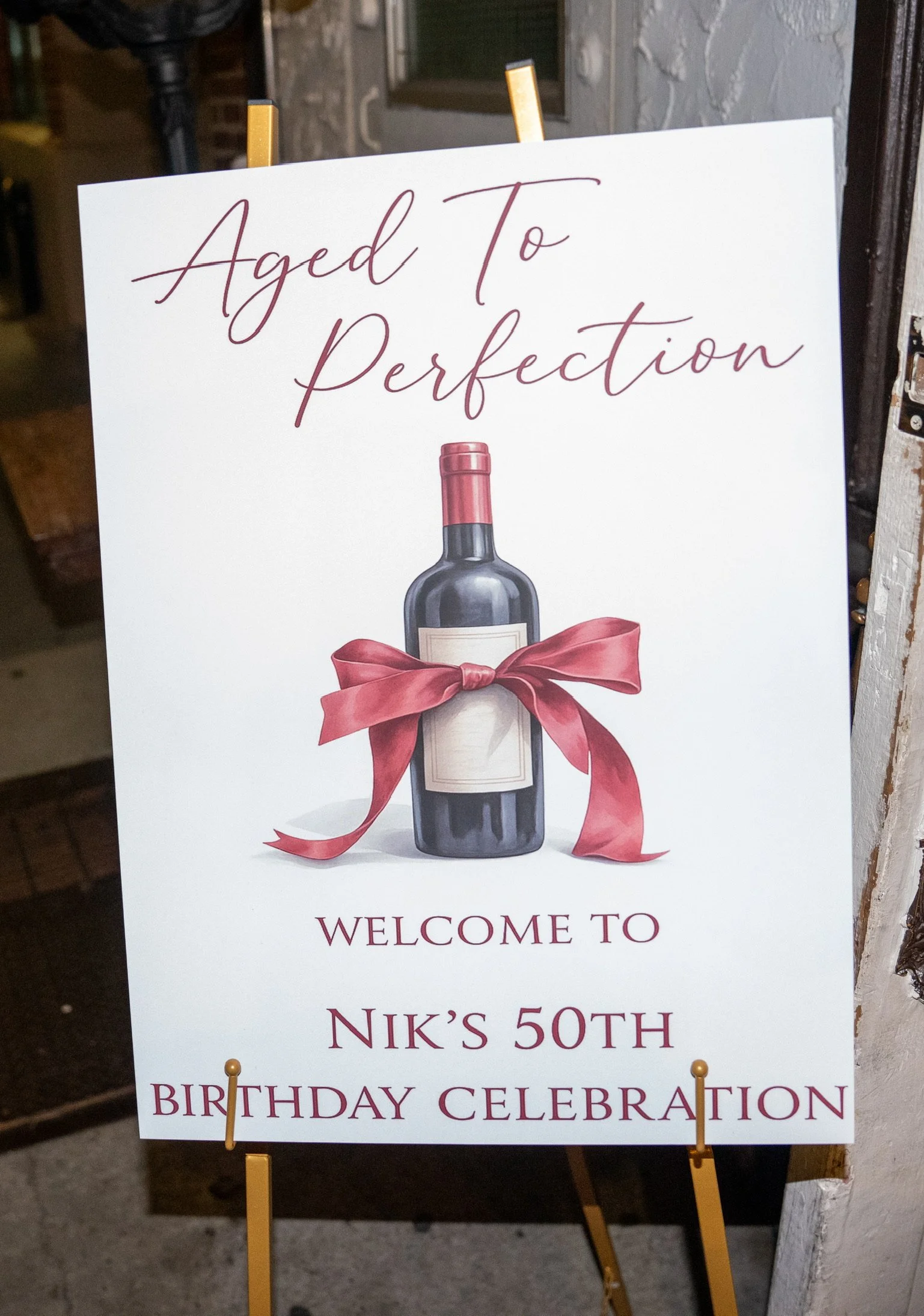 Sign celebrating Nik's 50th birthday with a wine bottle and a red ribbon.