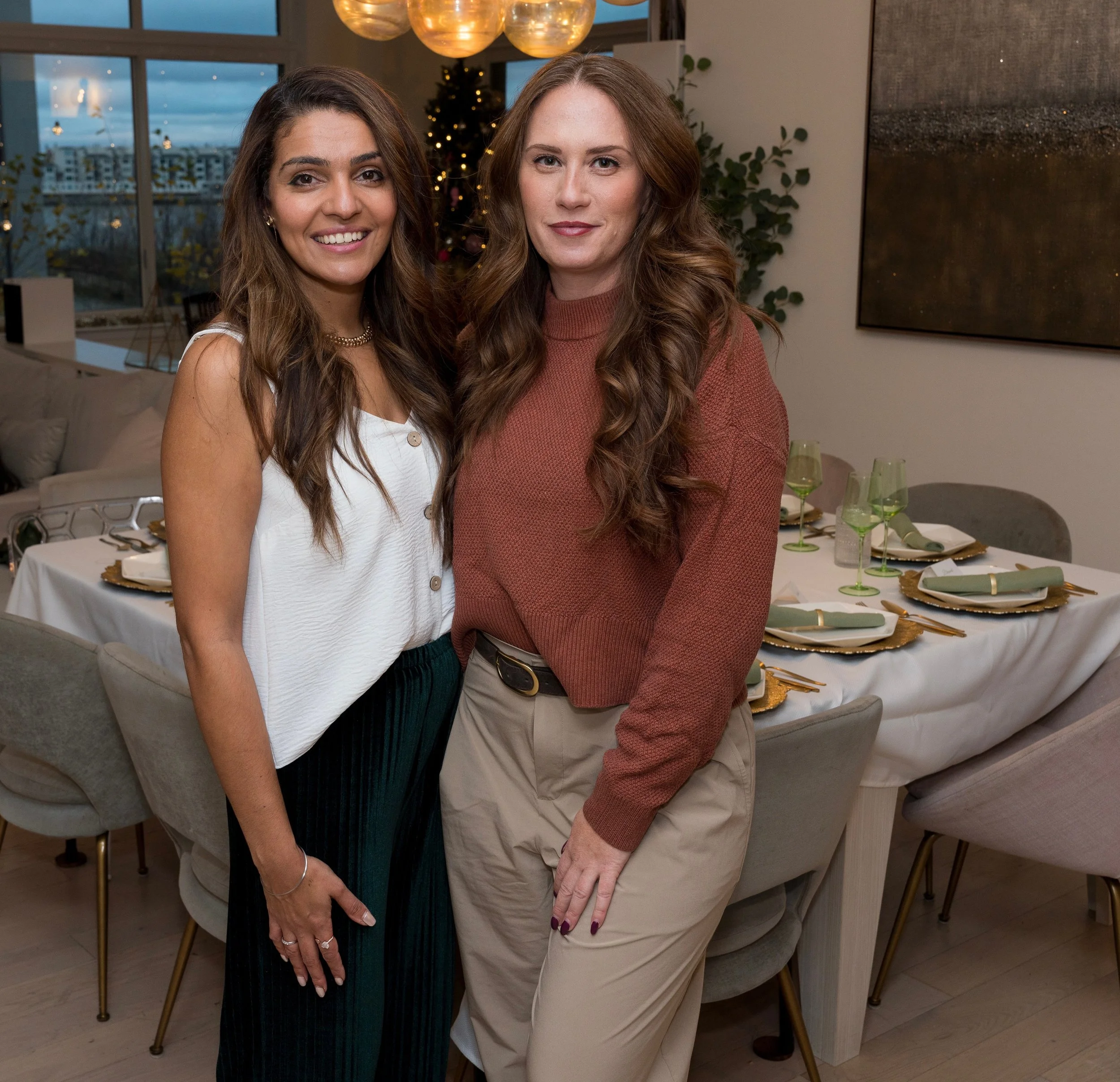 Two women standing together in a nicely decorated dining room with a large table set for a meal in the background.
