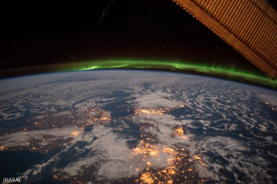 View of Earth from space showing the northern hemisphere, city lights, clouds, and the aurora borealis in the dark sky.