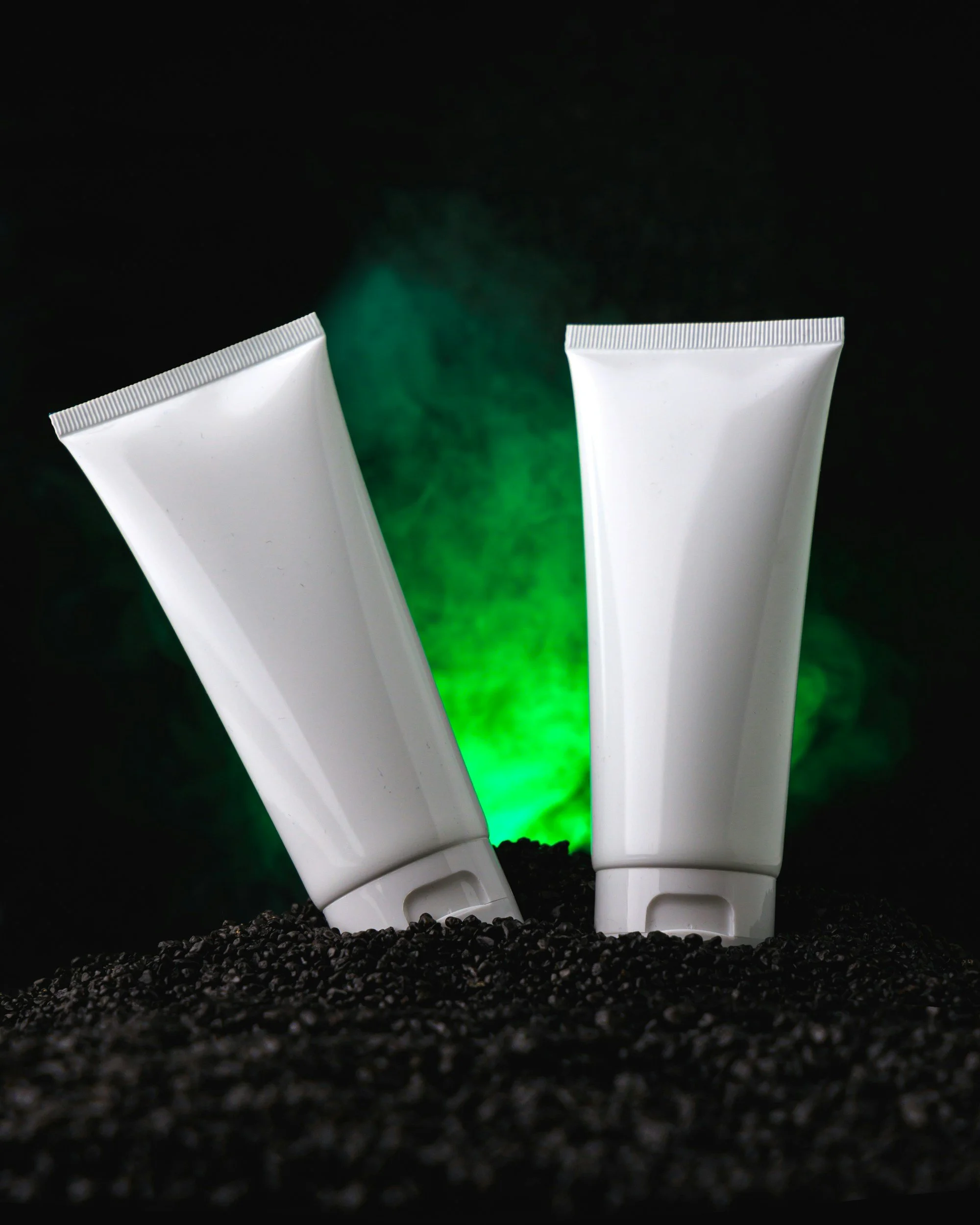 Two white tubes standing upright on black granular surface with a green mist or smoke in the background.