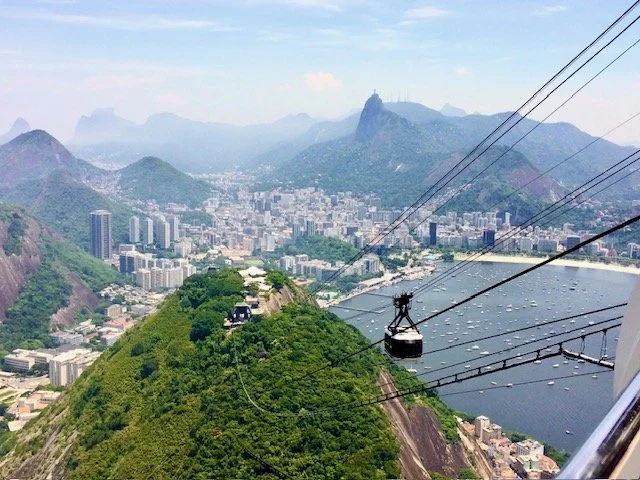 Cable car ascending Sugarloaf mountain with city buildings and a harbor in the background, overlooking Rio de Janeiro, Brazil.