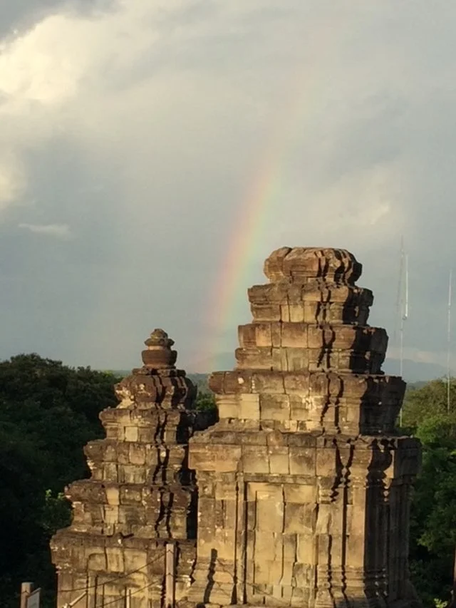 Ancient stone temple ruins with a rainbow in the sky behind.