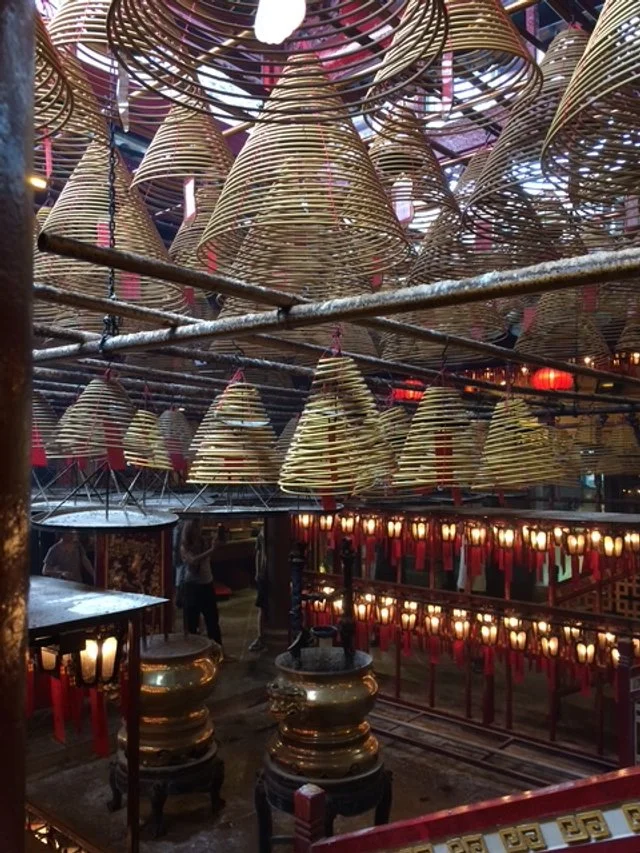 Interior of a traditional Chinese temple or shrine with hanging woven bell decorations, red lanterns, and gold-colored ornaments.