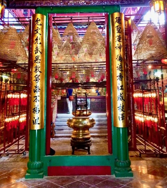 Interior of a Chinese temple with hanging lanterns, golden columns with Chinese calligraphy, and an altar with incense and offerings.