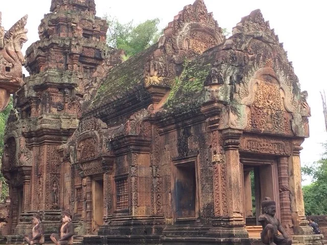 Ancient stone temple with detailed carvings and moss-covered roofs, flanked by stone statues of mythical creatures.
