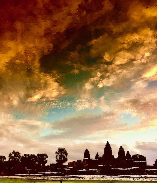 Colorful sunset sky over the silhouette of Angkor Wat temple in Cambodia with clouds and trees.