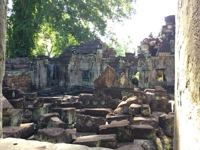 Ruins of an ancient stone structure surrounded by green trees, with fallen stones and crumbling walls.