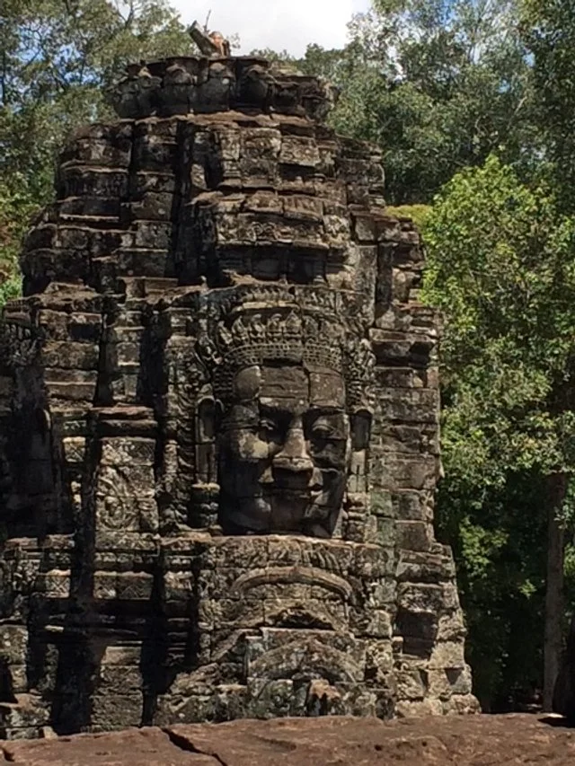Ancient stone temple ruins with a large carved face, surrounded by greenery.