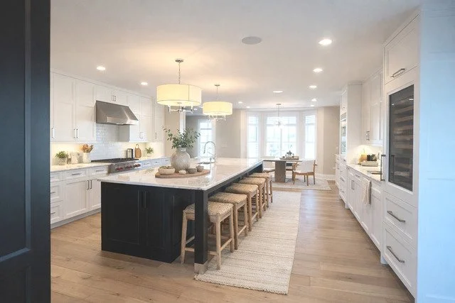 Modern kitchen with white cabinets, black island, wooden bar stools, and pendant lighting.