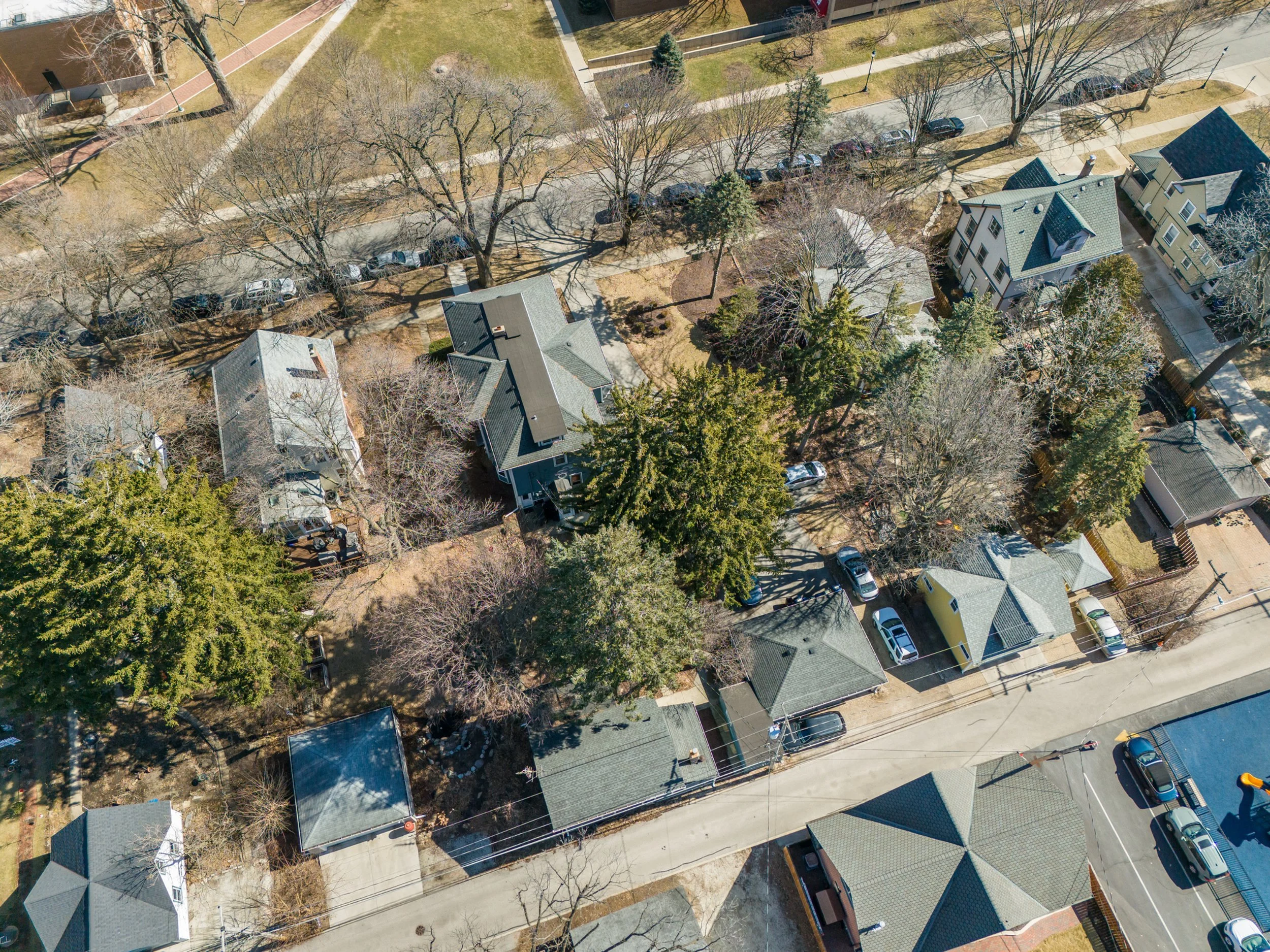 An aerial view of a residential neighborhood with houses, trees, streets, and parked cars.
