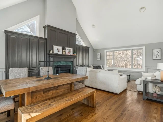 Living room with gray built-in cabinets, white ceilings, a large window, and a wooden dining table with a matching bench and chairs.