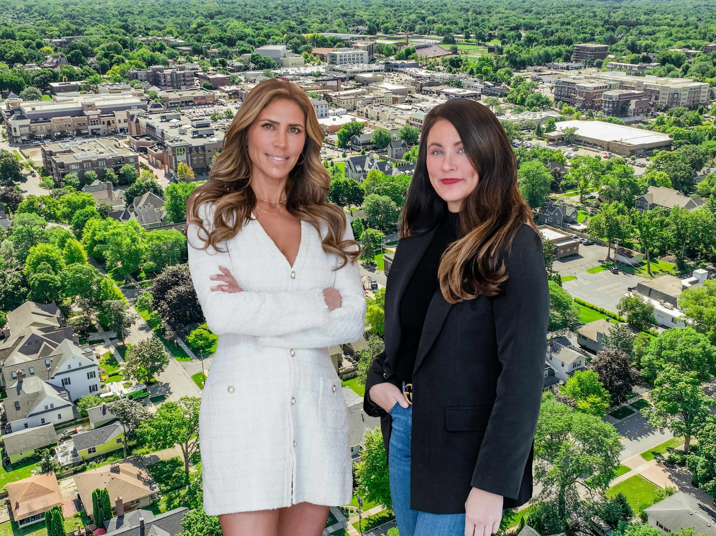 Two women standing outdoors with a cityscape and green trees in the background.