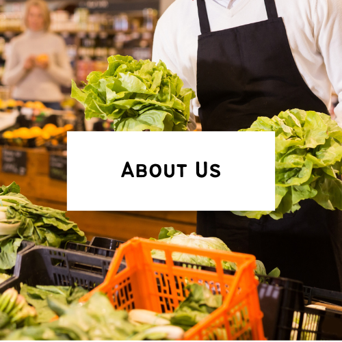 A person wearing a black apron shopping at a grocery store with fresh lettuce and vegetables on display.