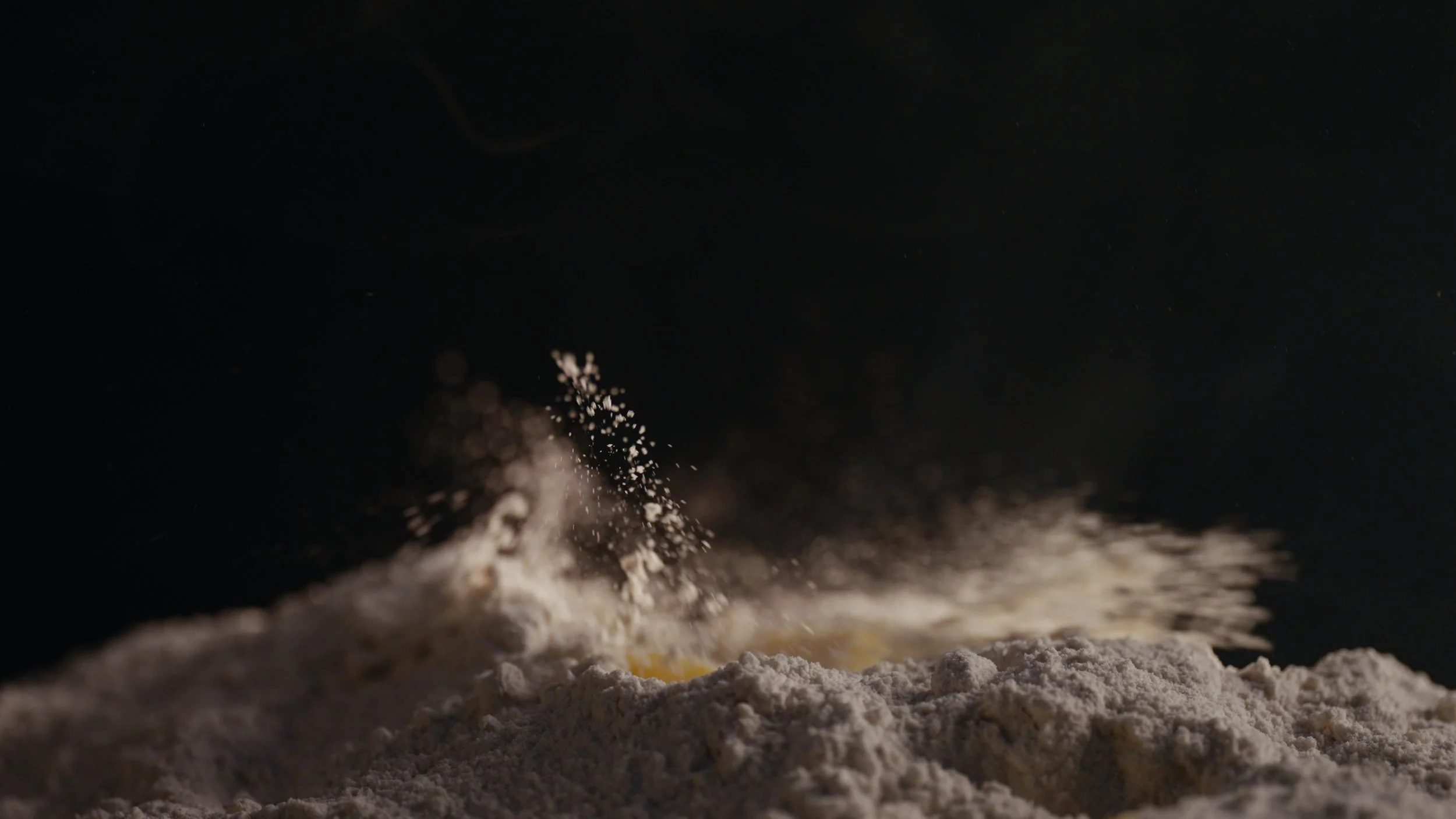 Close-up of flour being sprinkled onto a surface, captured in mid-air with a dark background.