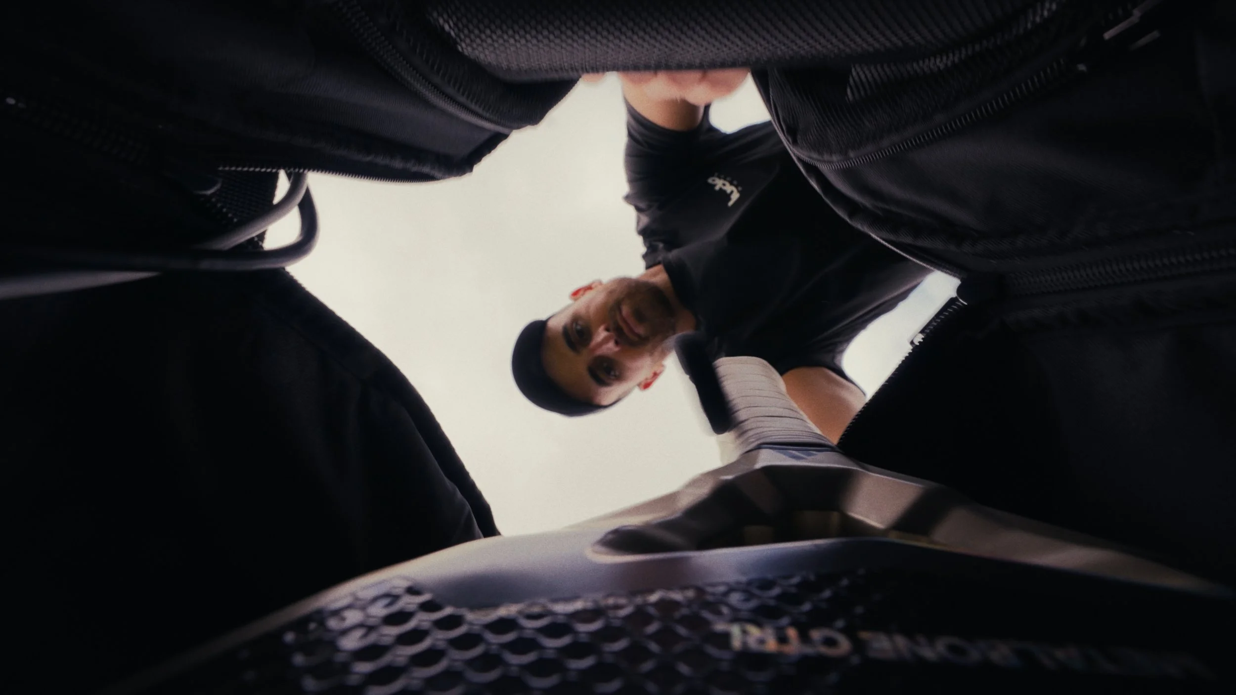 Man in black jacket and cap leaning over, looking down into an open motorcycle gas tank.
