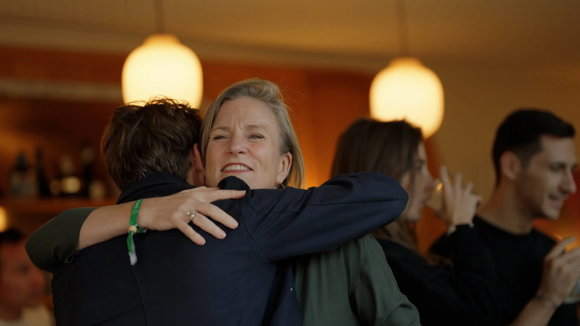A woman in a dark green shirt hugging a man with a band on his wrist, expressing emotion.