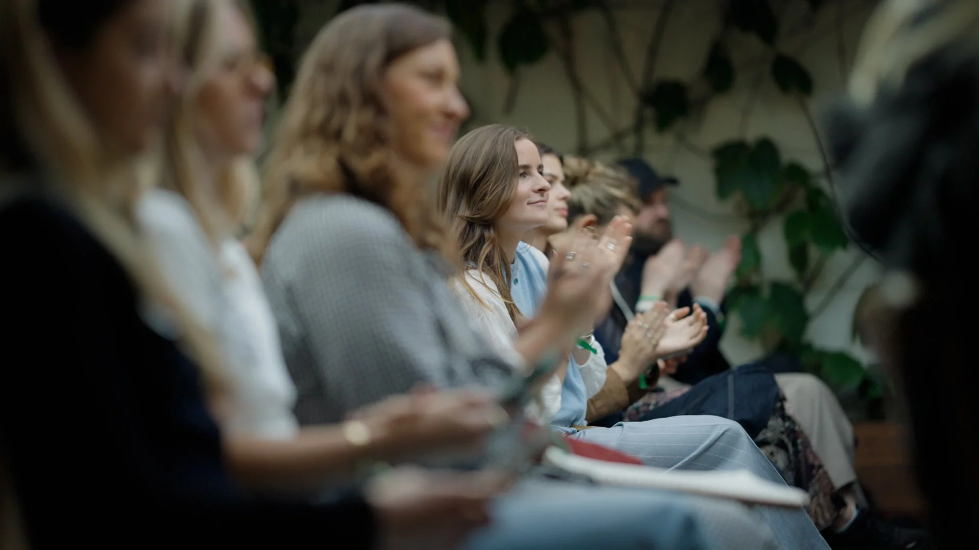 Group of people sitting in audience at an event, clapping and listening attentively.