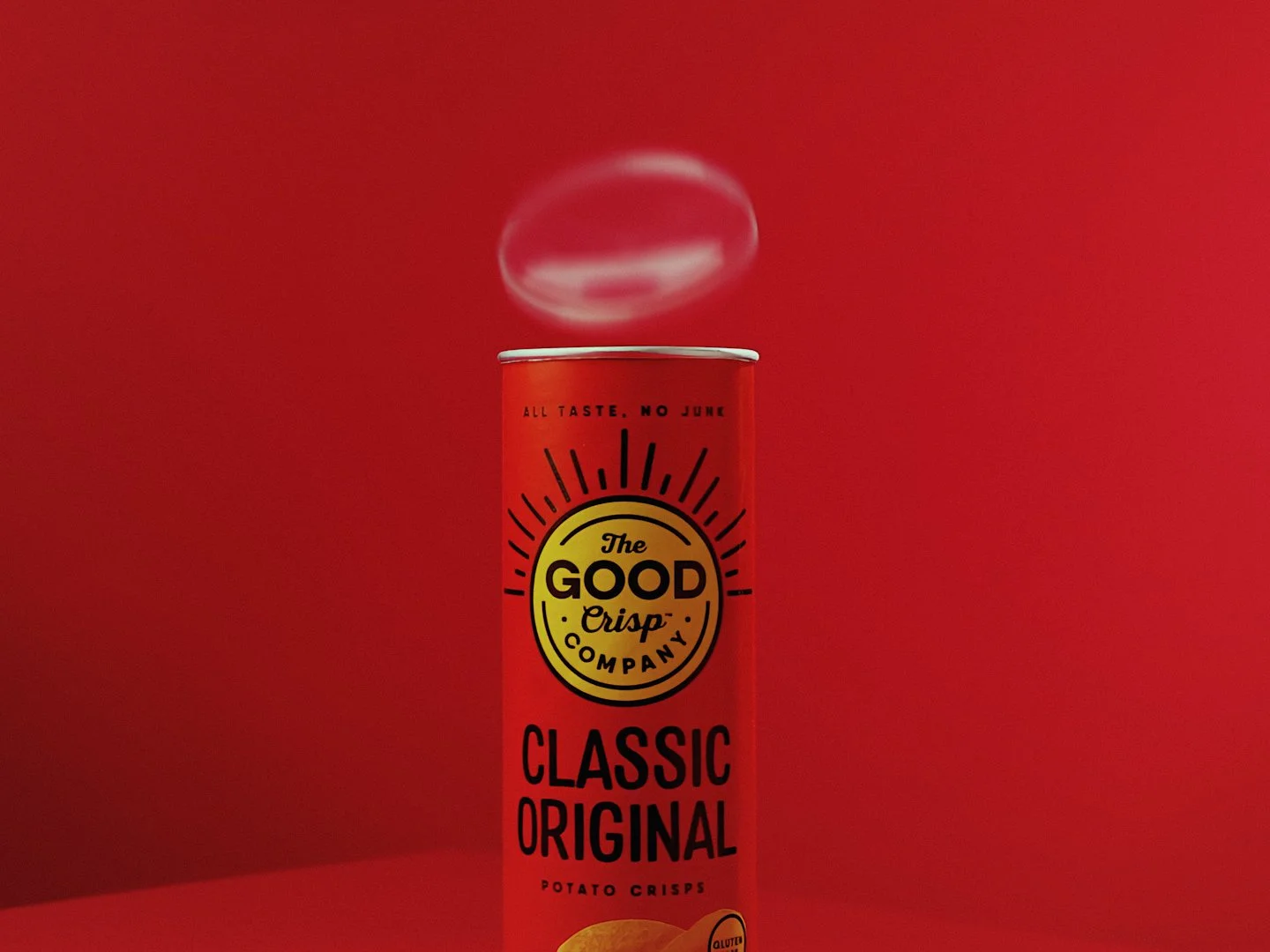 A red can of The Good Crisp Company Classic Original Potato Crisps with a bowl of potato chips in front, against a red background.