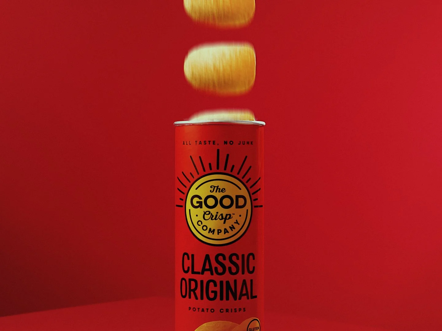 A can of The Good Crisp Company Classic Original potato crisps with some potato chips falling into the can against a red background.
