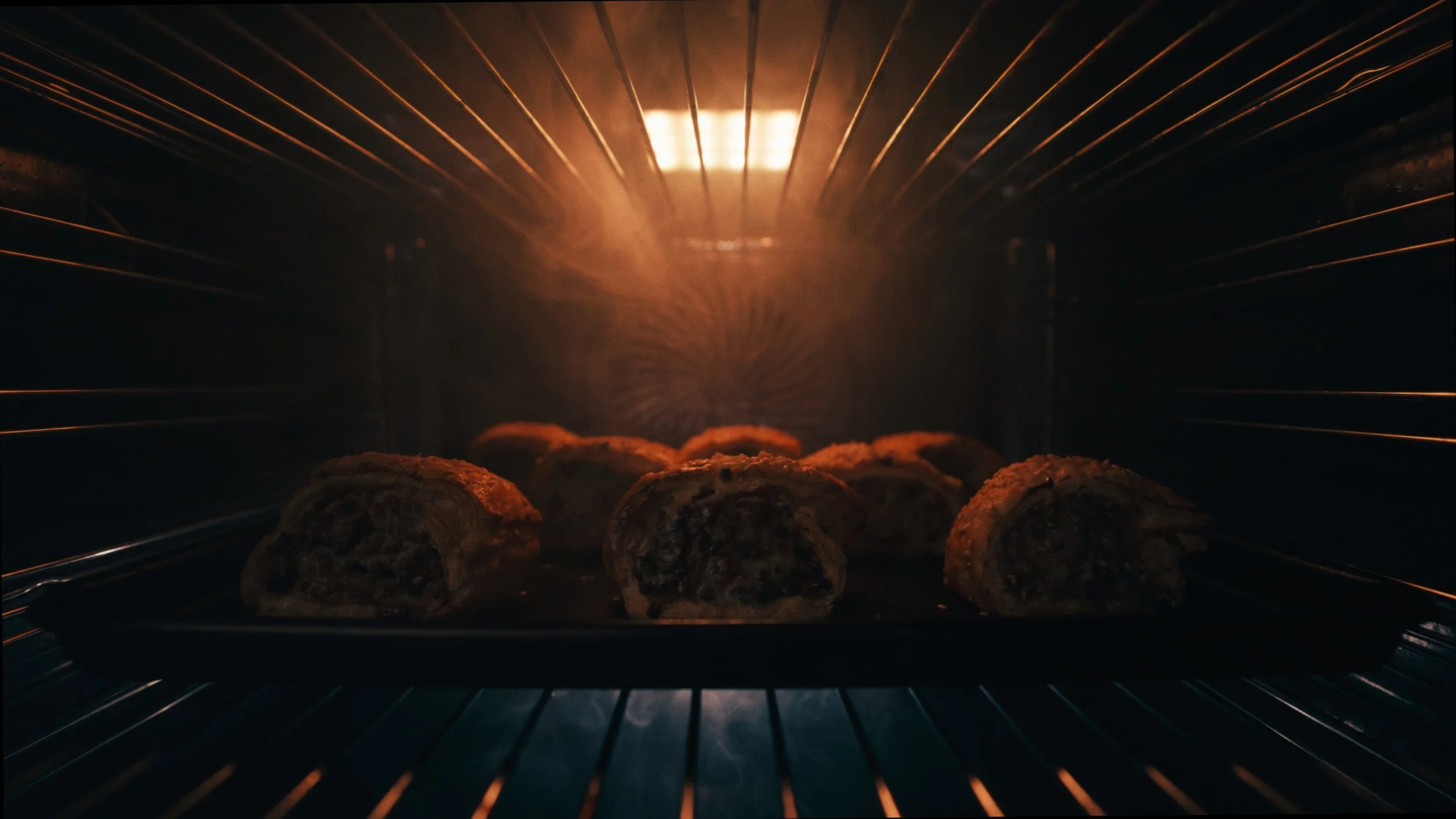 Meatloaf rolls baking in the oven on a metal tray inside the oven with glowing heat.