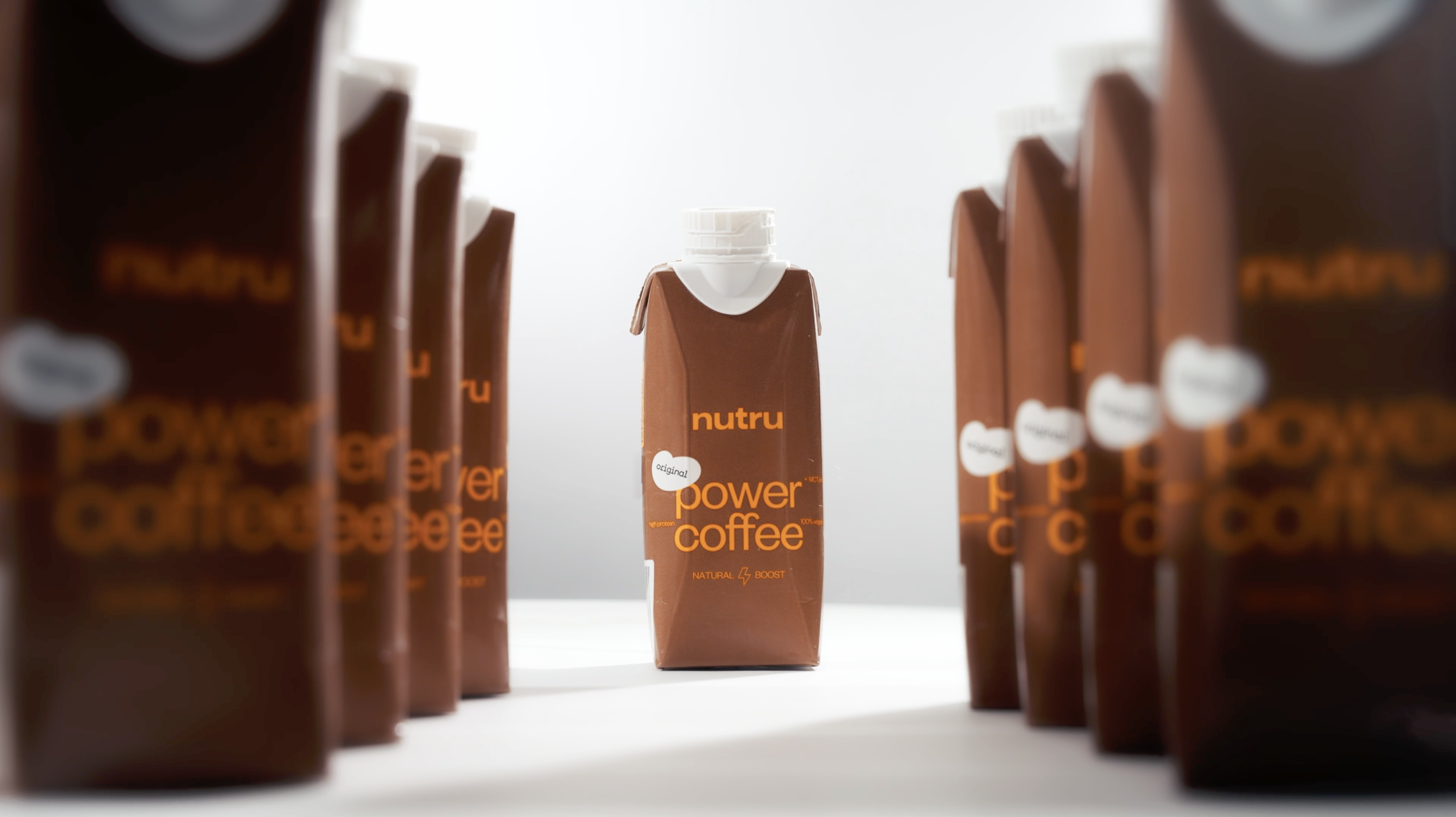A packet of Nutru Power Coffee in the center surrounded by multiple similar packets, all brown with orange text, on a white surface with a bright light background.