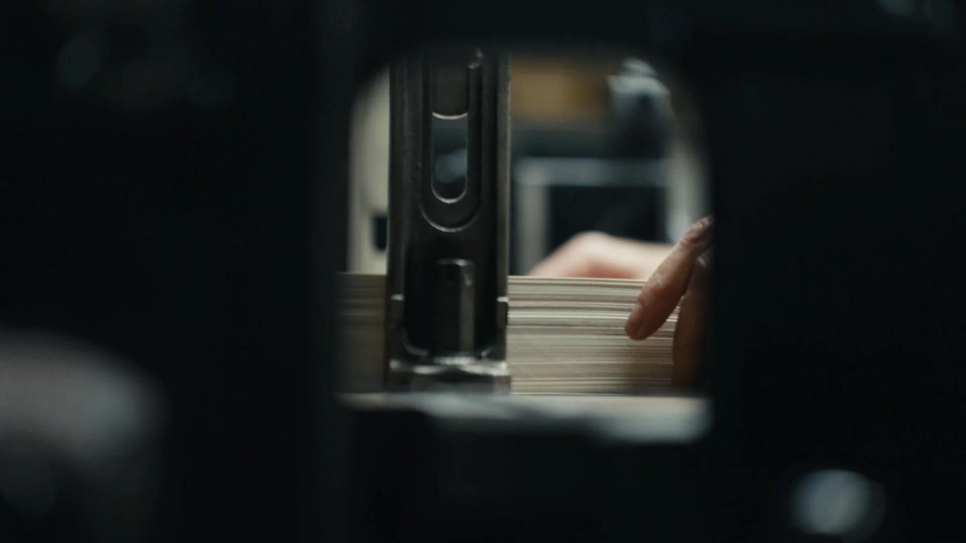 Close-up of a printing press or similar machine in operation, with a person's hand moving a stack of paper.