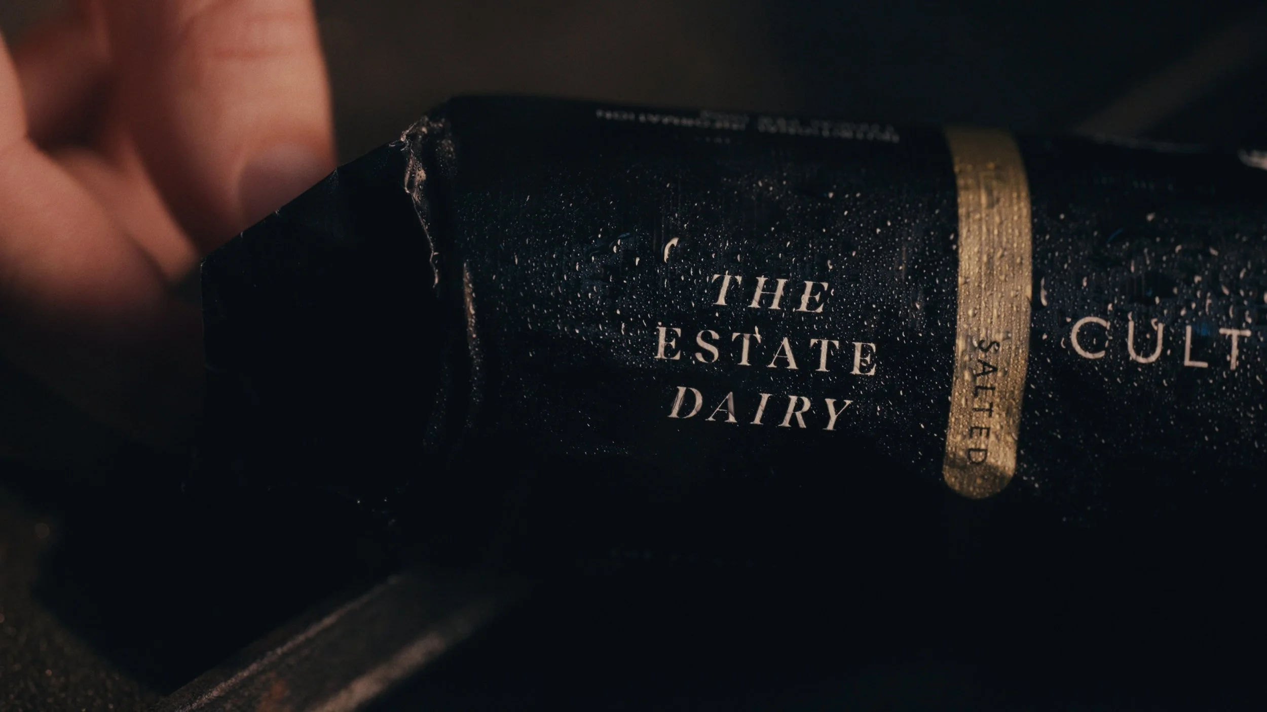 Close-up of a black package labeled 'The Estate Dairy' with water droplets on it.