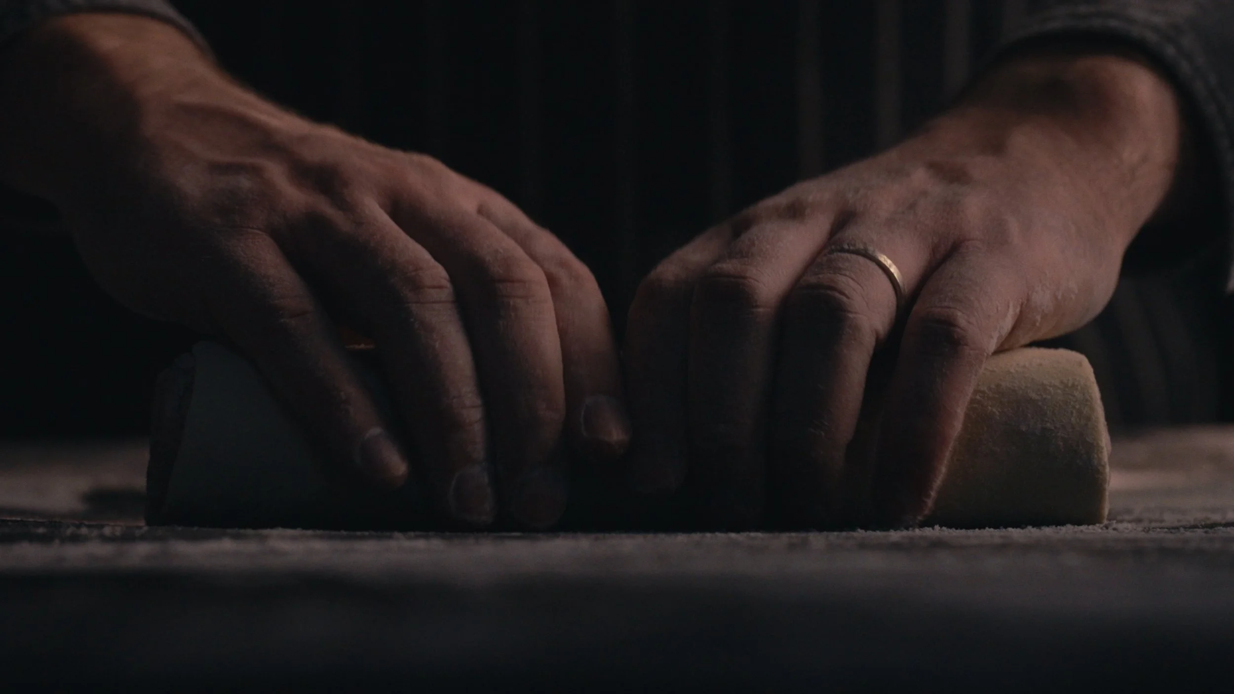 Close-up of hands kneading dough on a dark surface.