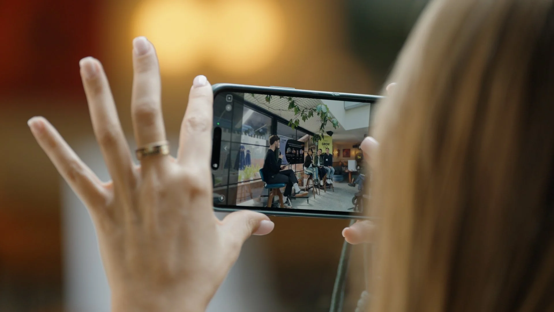 Person taking a photo of a panel discussion or presentation with a smartphone in an indoor setting.