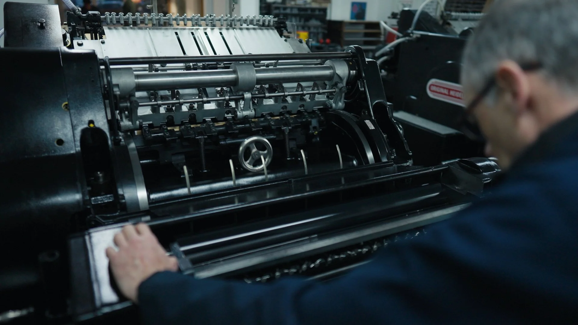 A technician working on a large mechanical machine, possibly a printing press or industrial equipment, in a workshop setting.