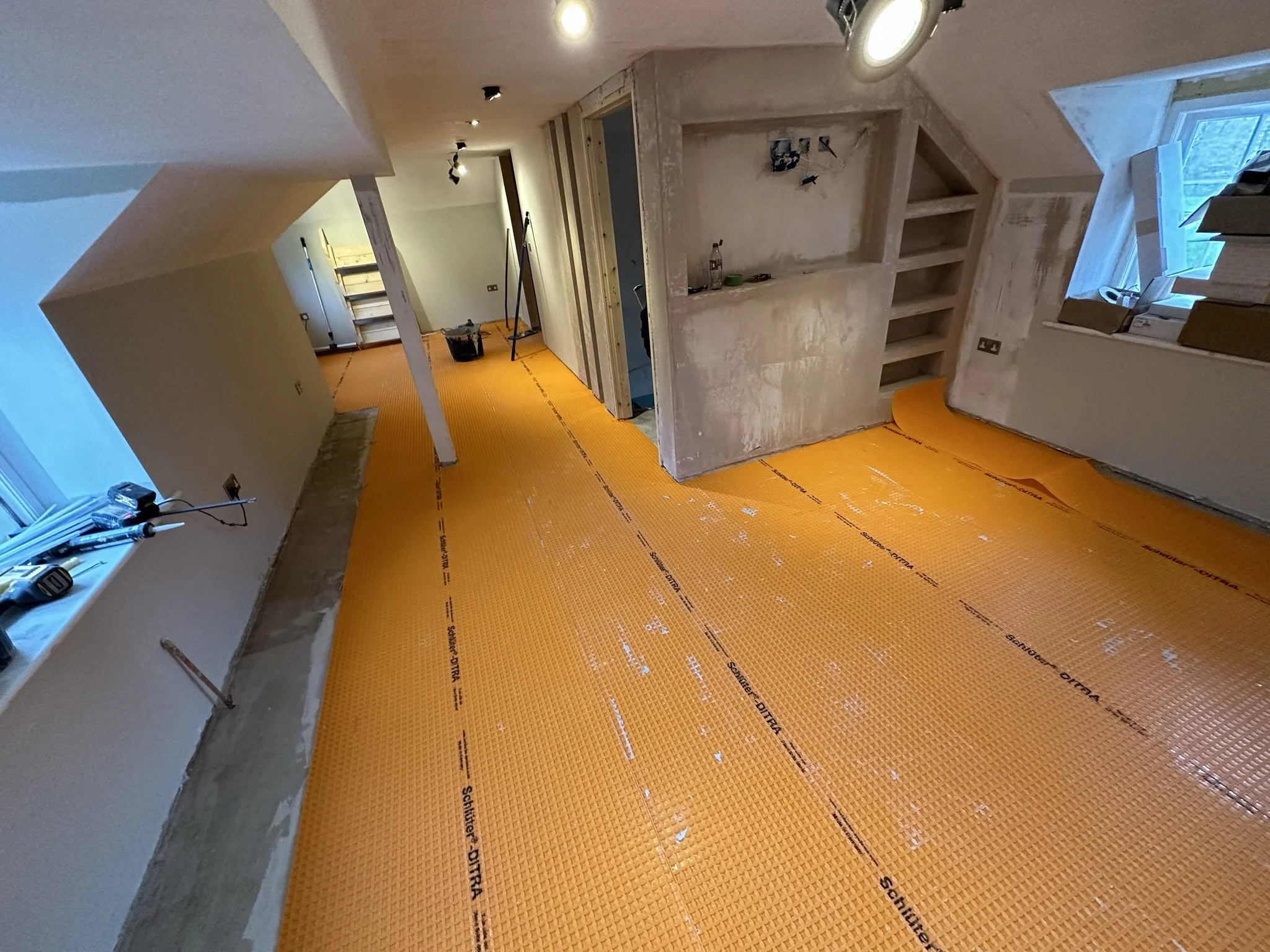 Interior of a house under renovation, with yellow insulation flooring, unfinished walls, tools, and construction materials visible.