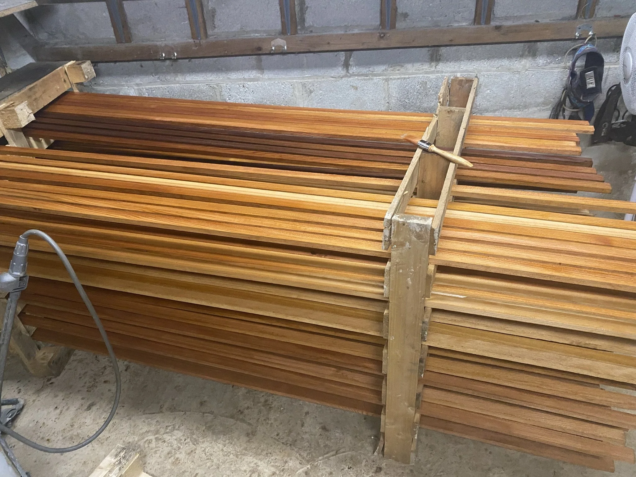 Wooden slats stored horizontally on a workbench in a workshop.