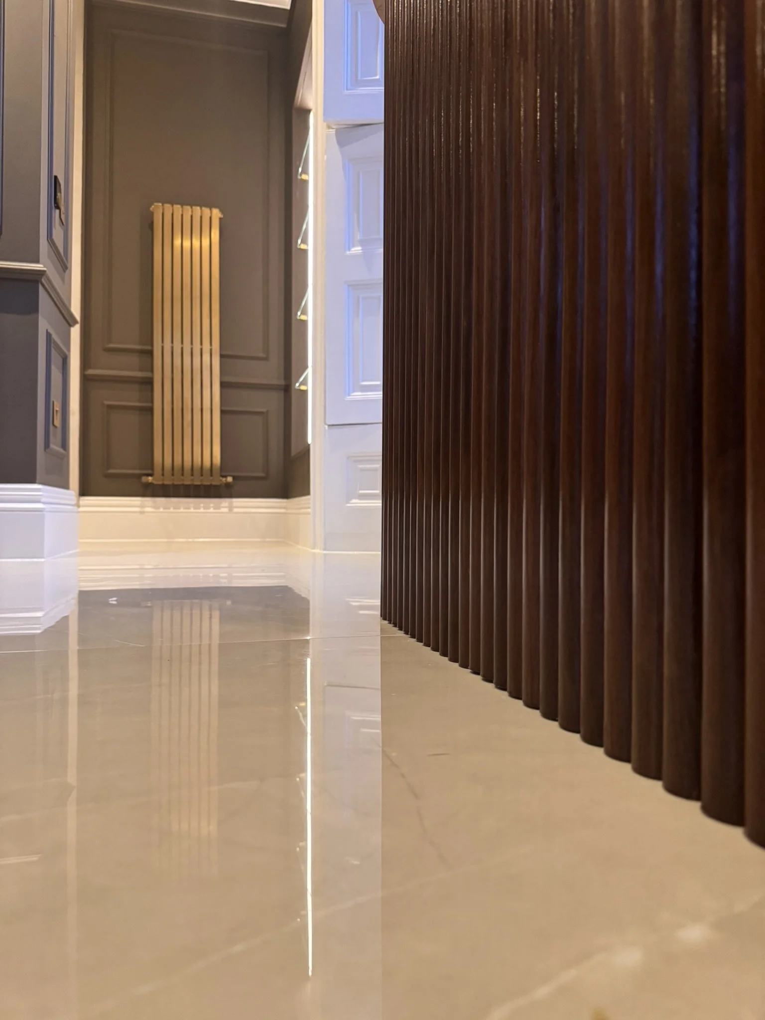Low-angle view of a modern interior corridor with beige tiled floor, grey walls, a white door, and a wooden vertical panel on the right side.