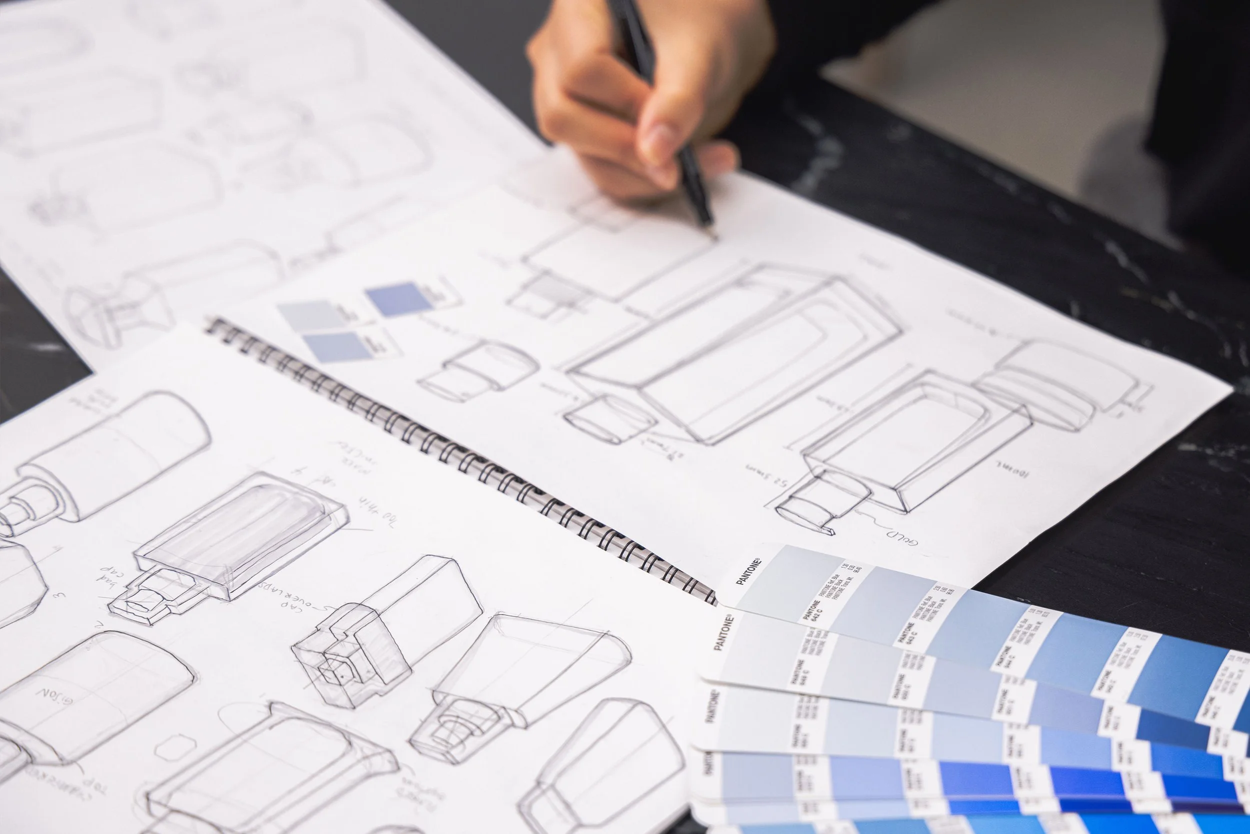 Person sketching product designs on paper with color swatches.