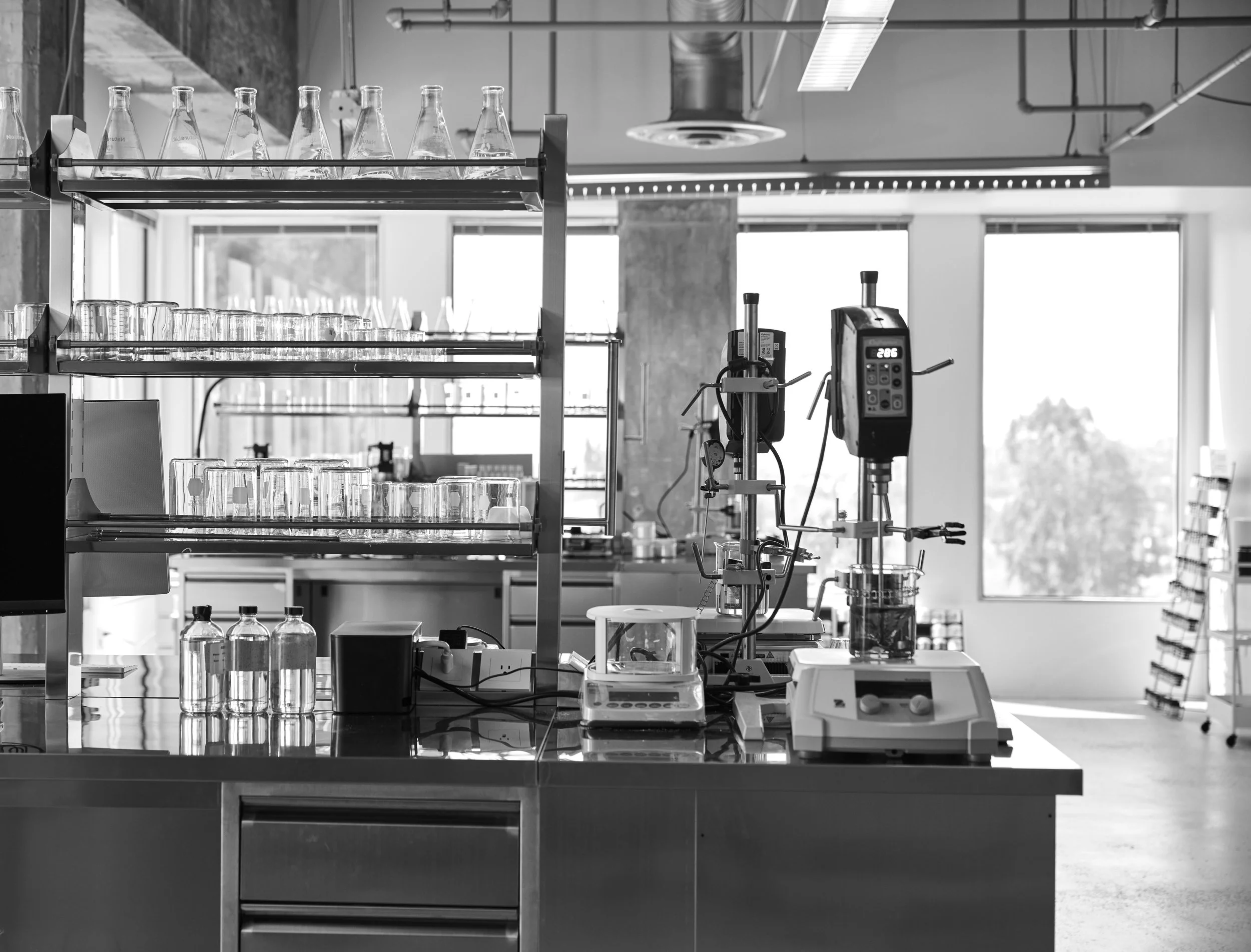 A modern laboratory with glassware, scientific instruments, and equipment on a shiny countertop, near large windows letting in natural light.