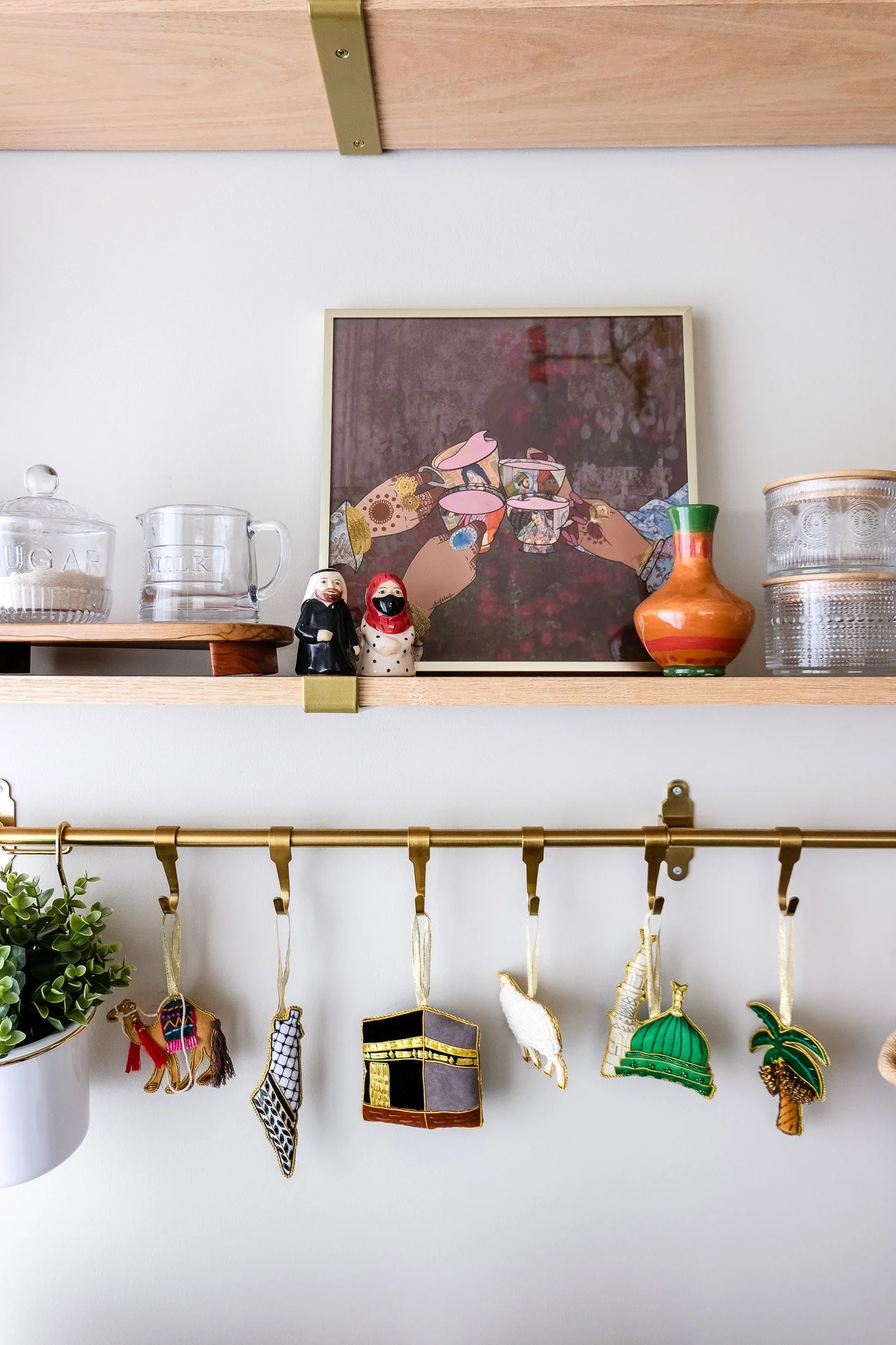 Decorative shelf with glass jars labeled 'sugar' and 'milk', framed artwork, small figurines, a colorful vase, and hanging ornaments.