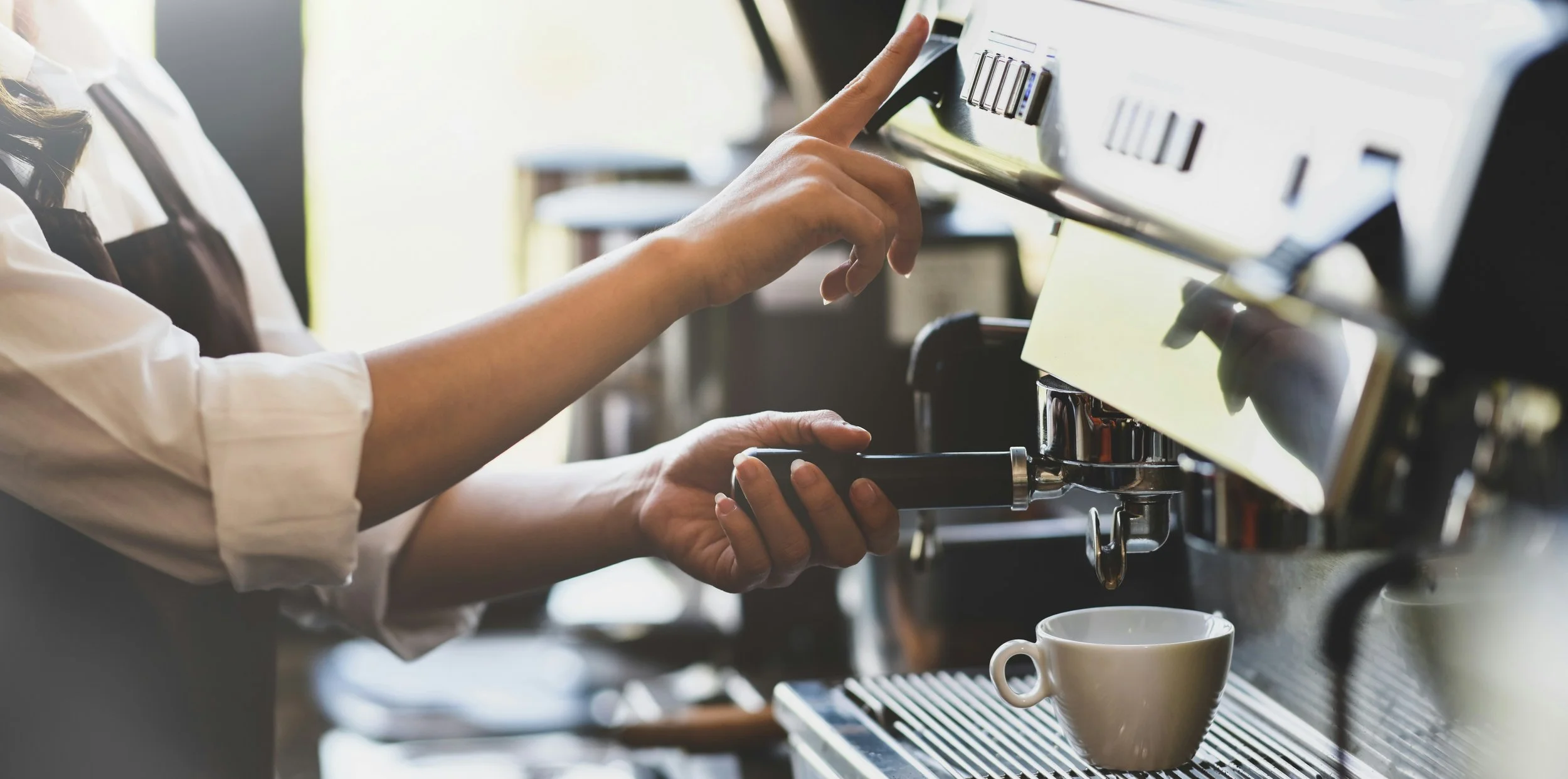 Person operating an espresso machine, preparing coffee with a cup underneath the spout.